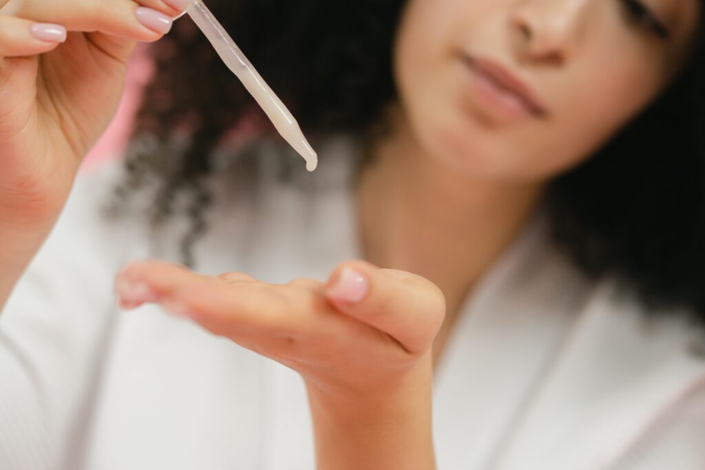 What Is The Best Makeup Primer For Mature Skin? Close-up of a woman applying skincare serum with a pipette, focusing on body care and cosmetic application.