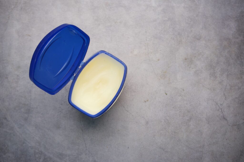 Is Vaseline Good For Dry Hands (Petroleum Jelly) Open blue plastic container with creamy substance on a solid gray background.