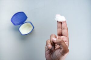 Is Vaseline Good For Dry Hands (Petroleum Jelly) A hand holding petroleum jelly on fingers, next to an open container. Skin care concept.