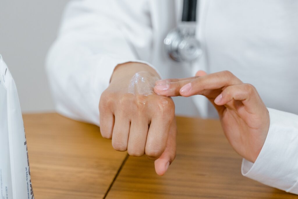 Why Are My Hands So Dry Even When I Moisturize? Here’s 4 Reasons Close-up of a doctor applying lotion on their hand, focusing on skincare.