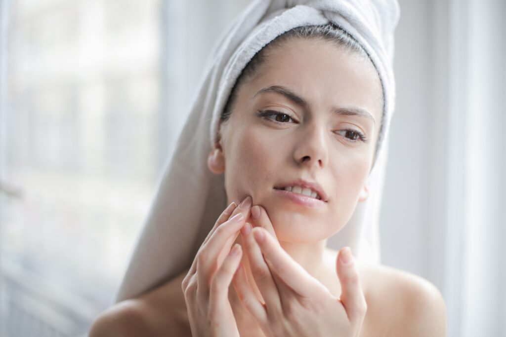 Does Oil Cleansing Help With Blackheads? Young woman with towel examining her face during skincare routine in a bathroom setting.