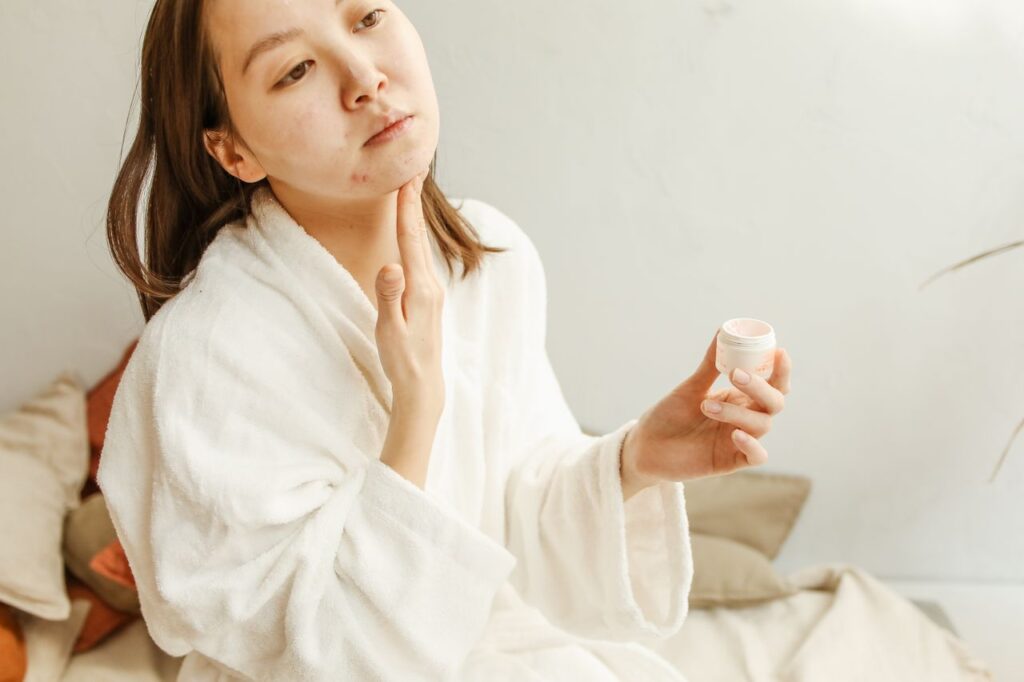 Best Skincare Routine for Acne-Prone Skin An adult woman in a bathrobe applies facial cream during her skincare routine indoors.