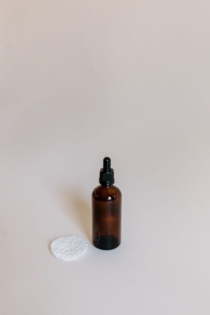 A minimalist composition featuring an essential oil dropper bottle with cotton pads on a white surface.
