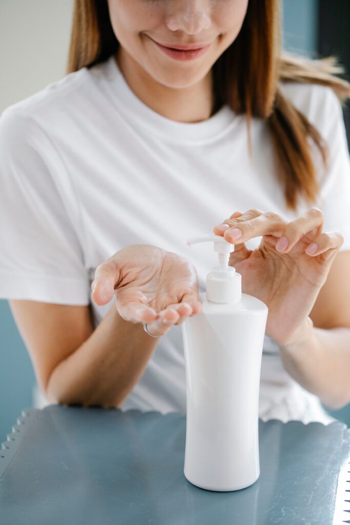 What is the Best Hand Lotion for Dry Cracked Hands Crop unrecognizable happy female millennial in casual clothes smiling while applying moisturizing lotion on hand using dispenser of white bottle during skin care routine