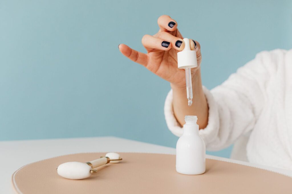 pexels photo 7321654 7321654 Hand in a bathrobe using a pipette to dispense skincare product into a white bottle.