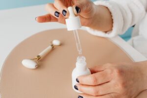 Can Niacinamide Cause Purging? Close-up of hands using serum dropper with jade roller, perfect for skincare routines.