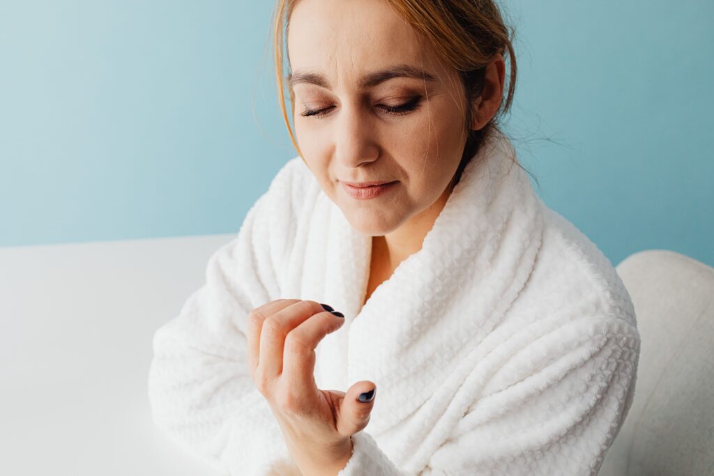 Adult woman in a bathrobe admiring her newly manicured nails, embracing a moment of self-care.