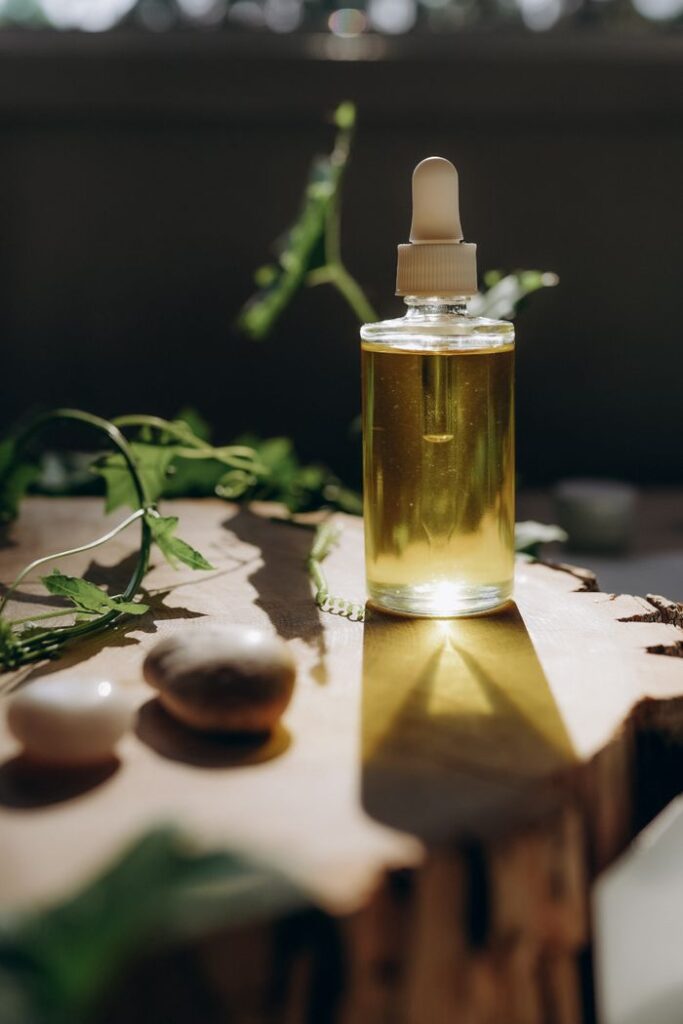 How to Do Oil Cleansing With Coconut Oil Step by Step A clear bottle of aromatic oil on a wooden surface, surrounded by natural elements and sunlight.