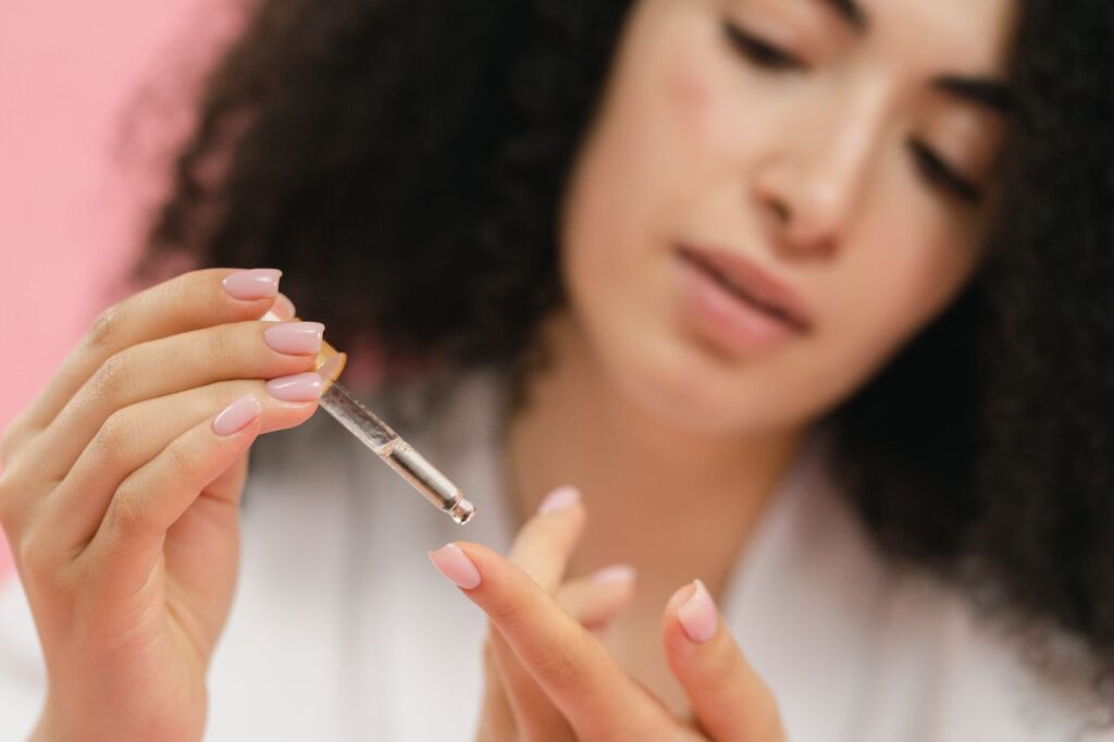 pexels photo 9775216 9775216 Close-up of a young woman applying skincare serum with a pipette against a pink background.