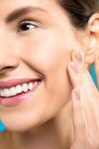 How to Get Glowing Skin Naturally? A close-up portrait showing a woman gently touching her cheek, showcasing healthy skin and a vibrant smile.
