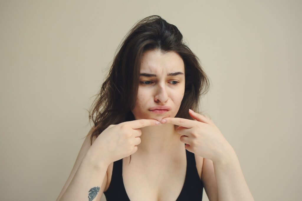 pexels photo 5588024 5588024 A woman looks at her skin with concern, touching her chin, worried about acne.