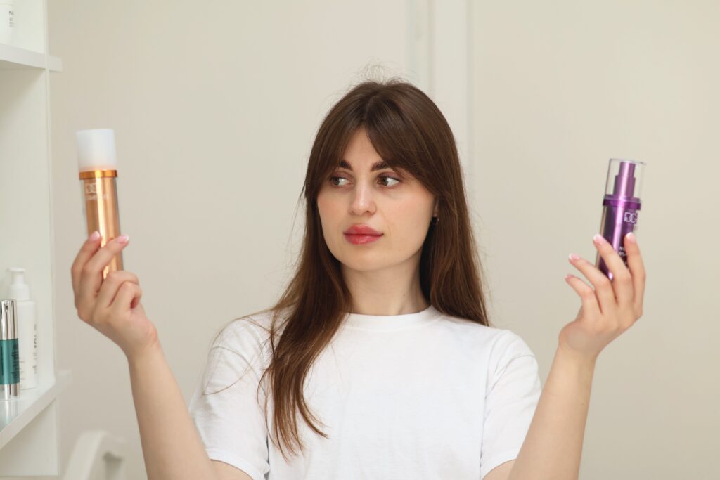 pexels-photo-17891760-17891760 A young woman compares two cosmetic products while standing indoors, unsure of which to choose.