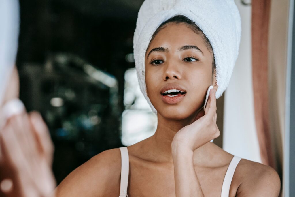pexels-photo-5938626-5938626 Ethnic female with mouth opened cleaning face with cotton pad while looking at mirror during daily beauty care